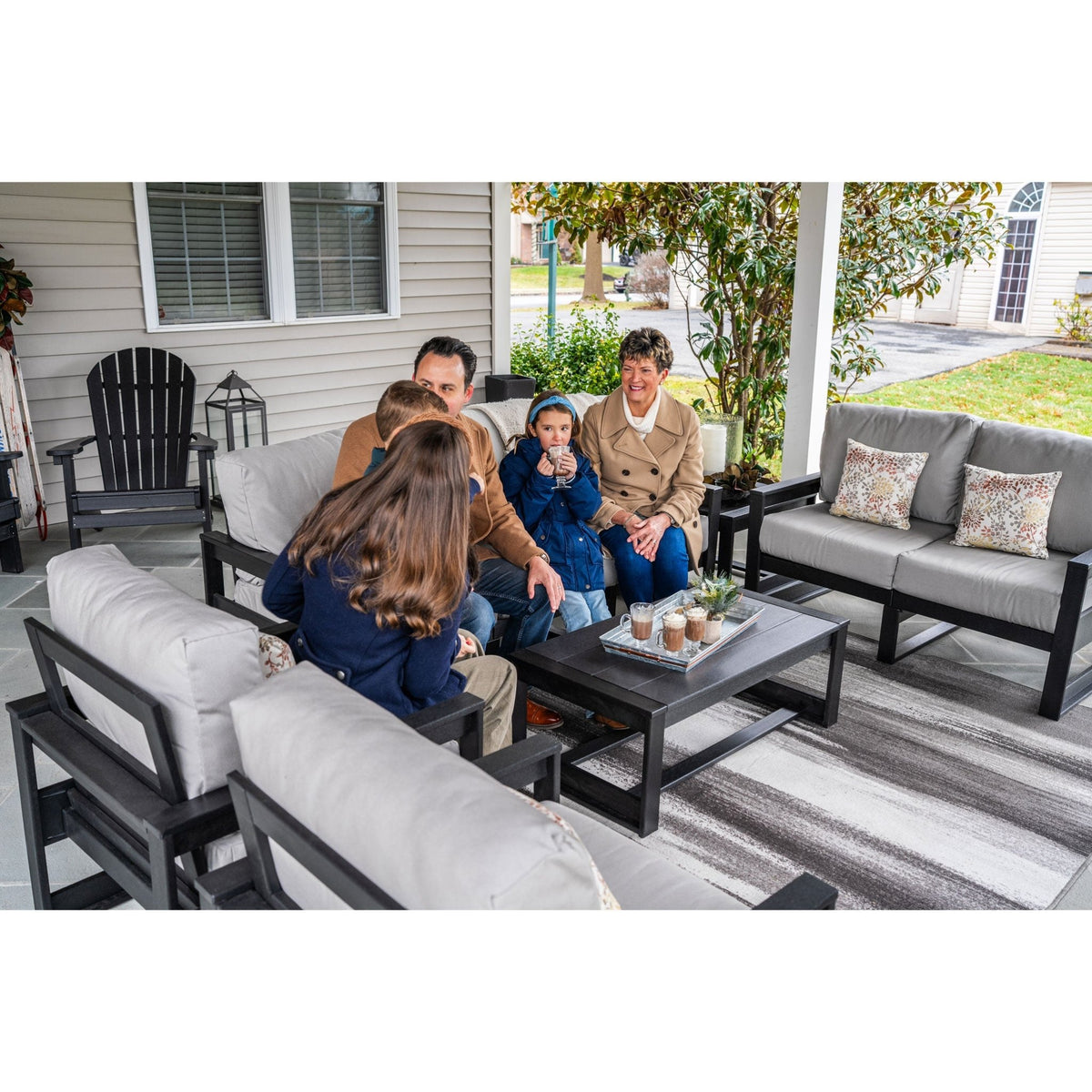 Family talking on black poly patio sofas with gray cushions around a coffee table on a porch