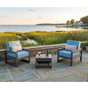 Two mid-century modern poly patio chairs with blue cushions and a square side table overlooking a marsh