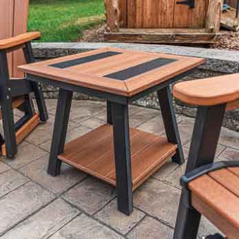 Square poly end table with cedar and black striped top and lower shelf between two patio chairs