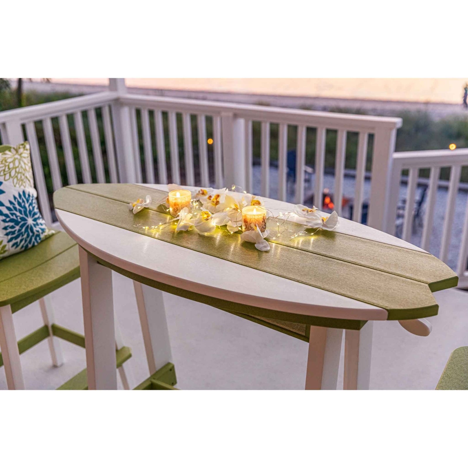 Lime green and white surfboard shaped bar table with two bar chairs on a beachfront porch at sunset