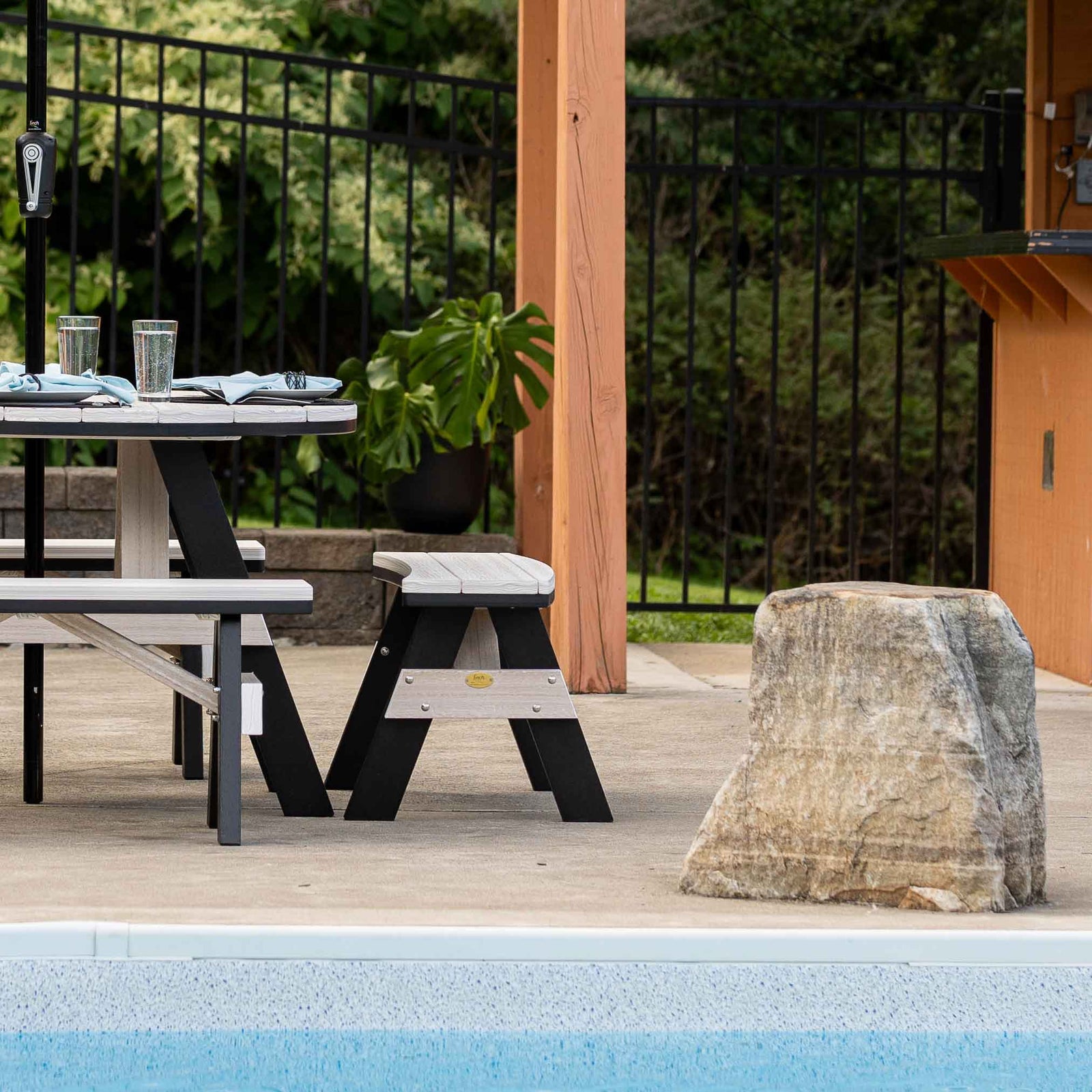 Weatherwood and black poly bench with A frame legs set beside a patio dining table near a pool