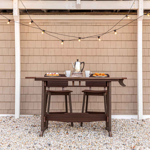 Dark brown recycled poly counter table with two backless stools tucked underneath on a gravel patio with string lights