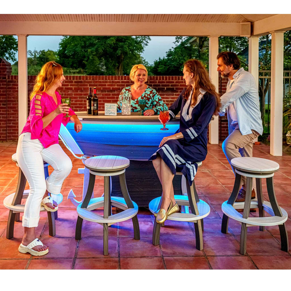 Friends gathered around a boat shaped poly patio bar with blue LED lighting and round swivel bar stools on a covered patio