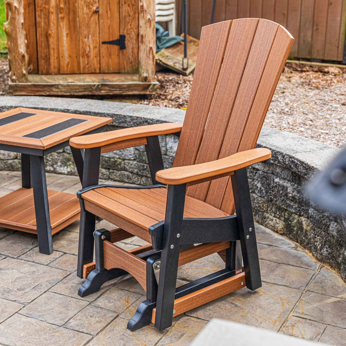 Antique mahogany and black poly glider chair with fan back, wide arms and gliding base on a stone patio