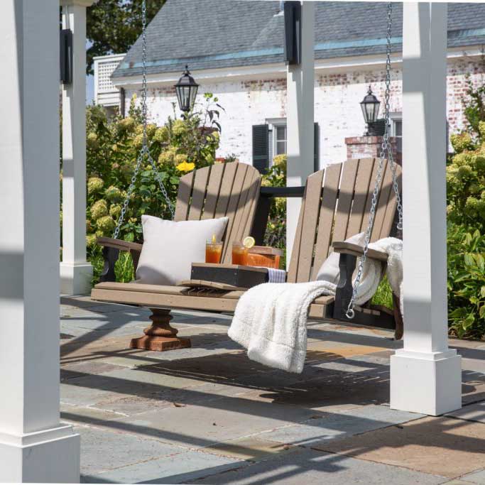 Weatherwood and black poly fan back porch swing with flip down console holding drinks under a white pergola