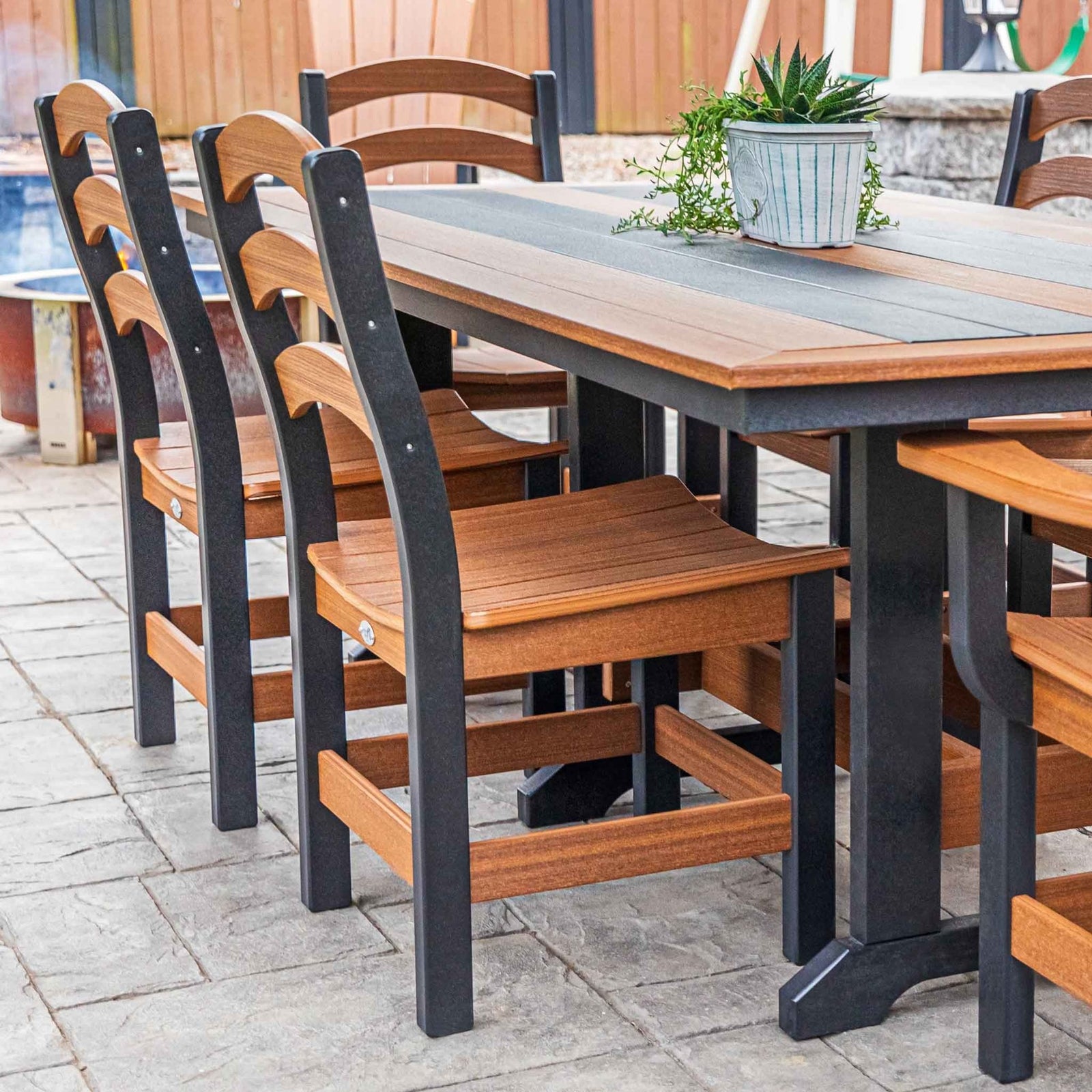 Cedar and black poly ladder back dining chairs around a long outdoor table on a stone patio
