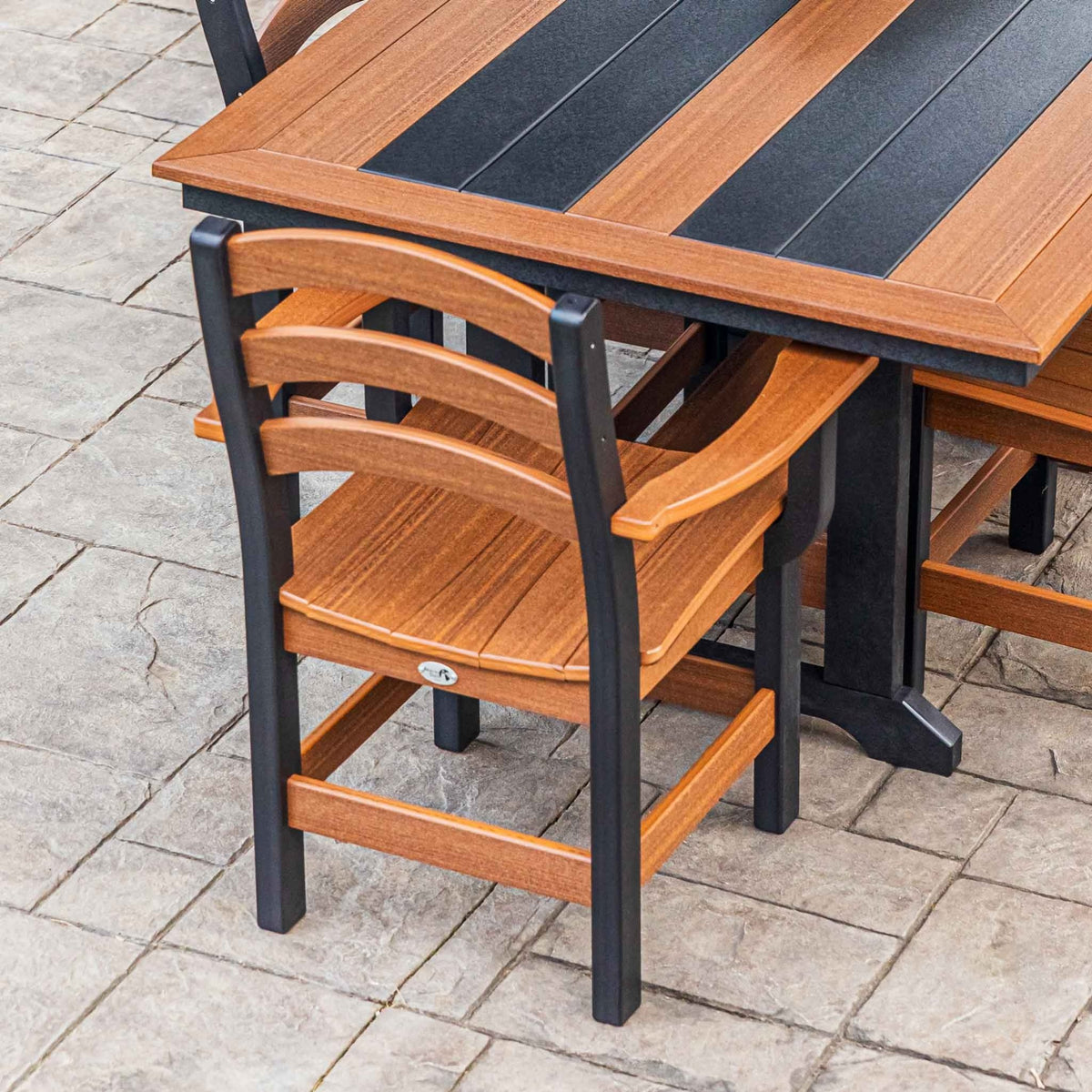 Close view of a cedar and black poly dining arm chair beside a two tone patio table and bench