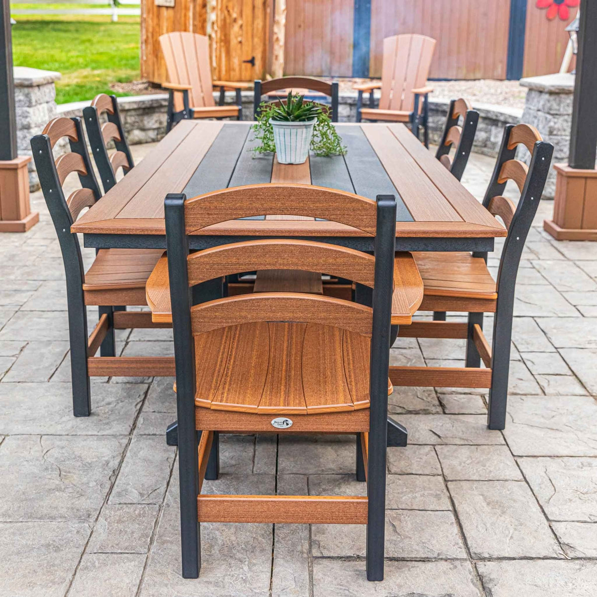 Long cedar and black poly outdoor dining table with six ladder back chairs on a stamped concrete patio