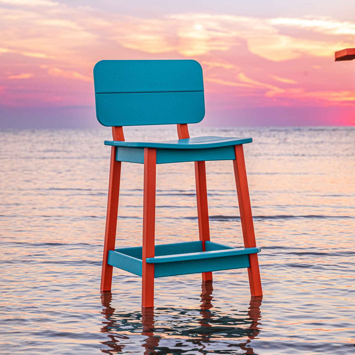 Turquoise saddle counter stool with orange legs and a wide back panel standing in the surf at sunset