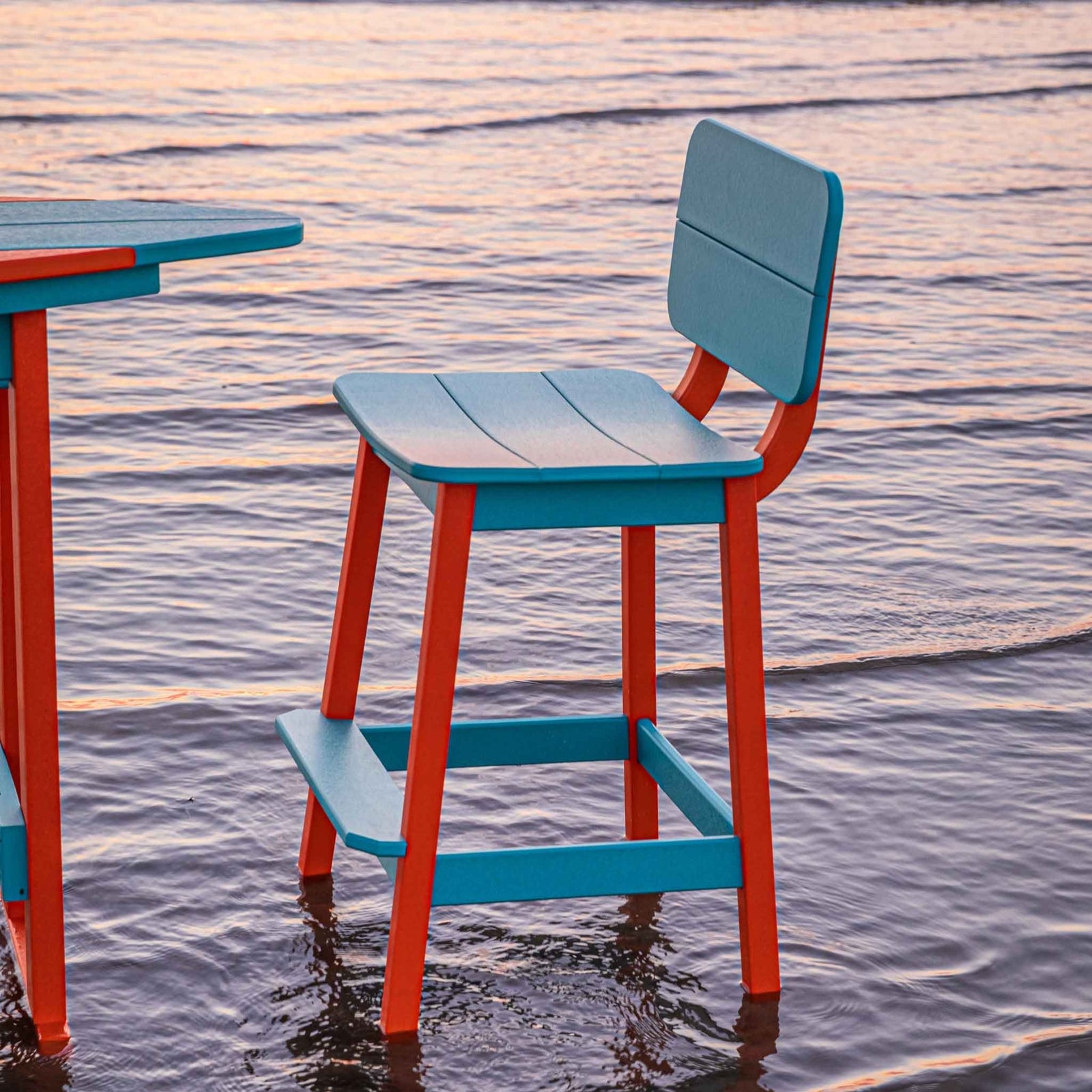 Aqua and orange counter stool with a scooped saddle seat and low back beside a poly table in the water