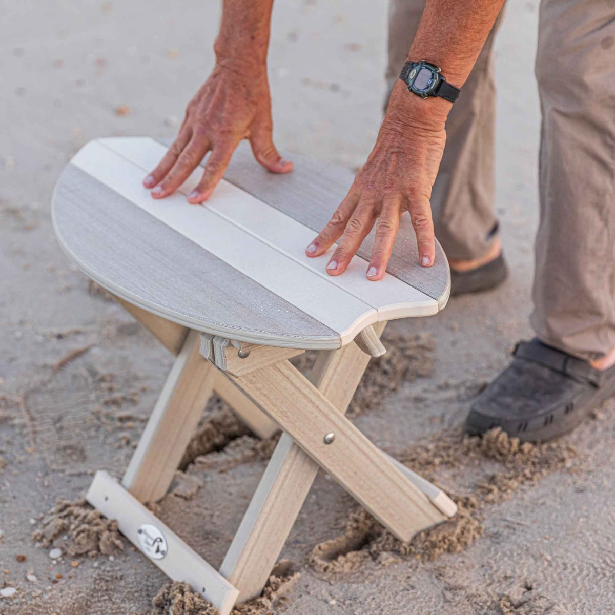 Set up driftwood gray surfboard folding table on the beach with a hand steadying the top