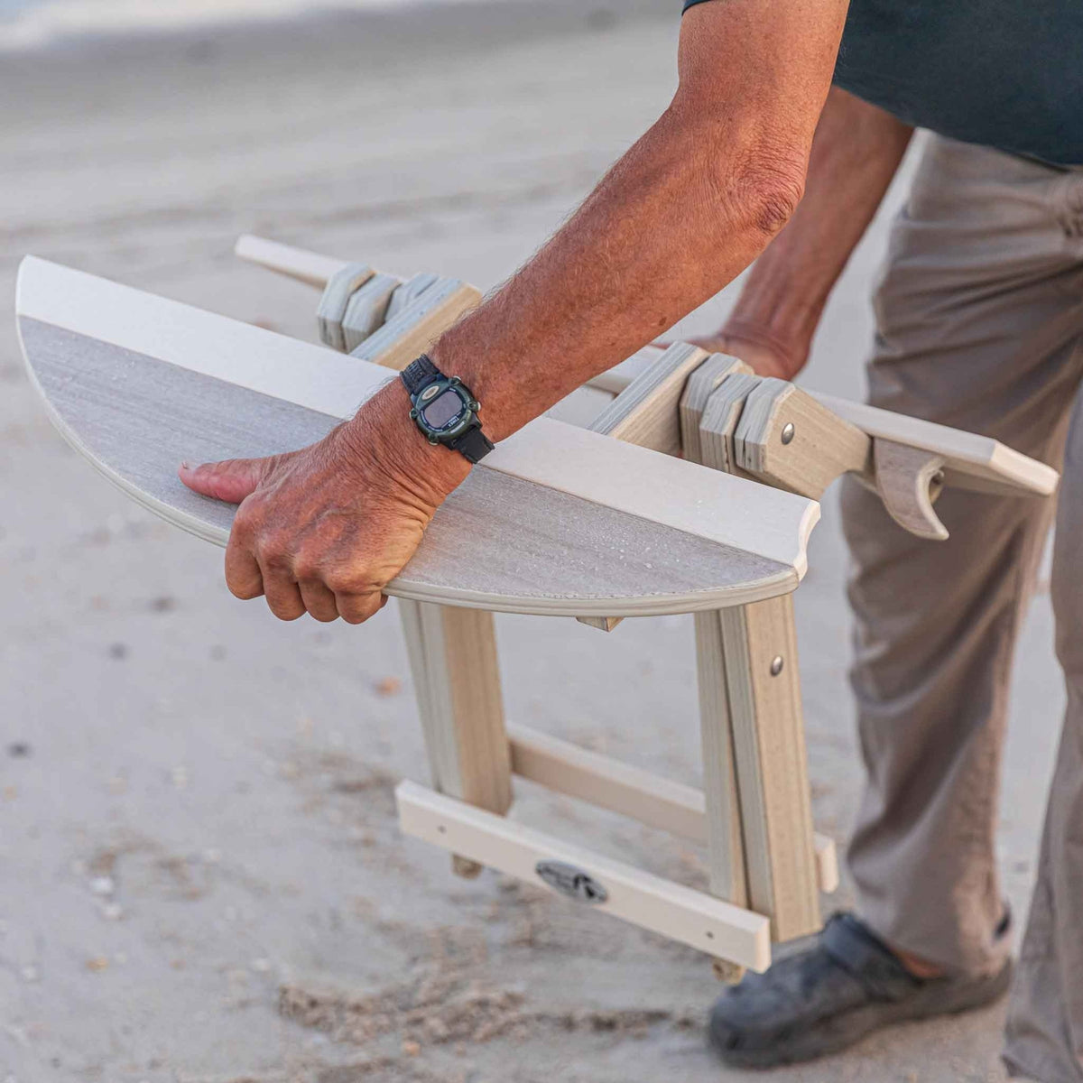 Close view of hands unfolding the light gray surfboard shaped poly folding end table on the beach