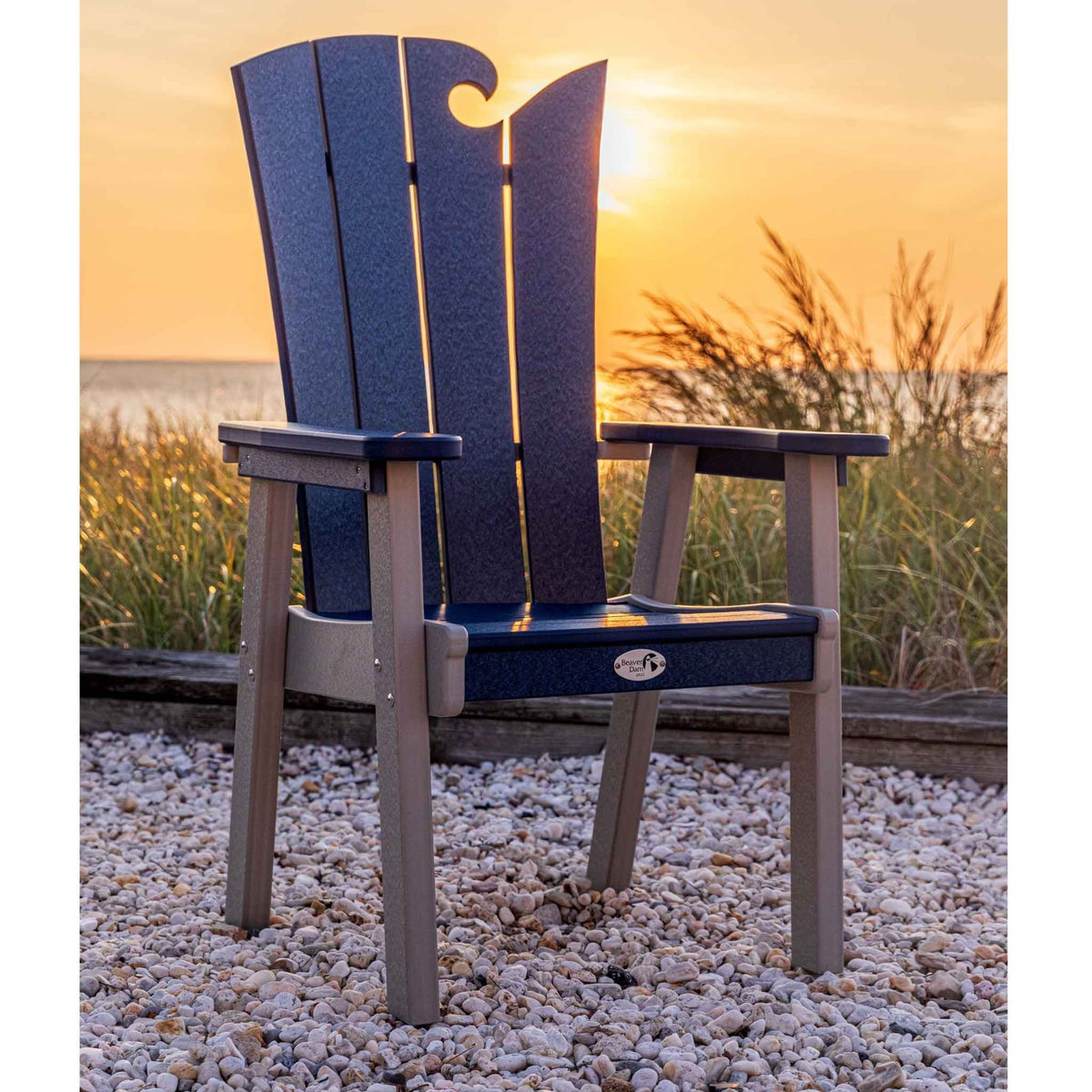 Navy and gray wave back poly dining chair on a gravel patio with beach grass and sunset behind