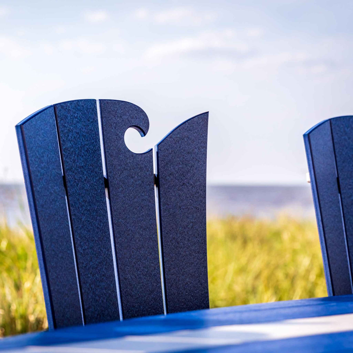 Close-up of the navy wave cutout crest rail on poly patio chair backs with beach grass behind