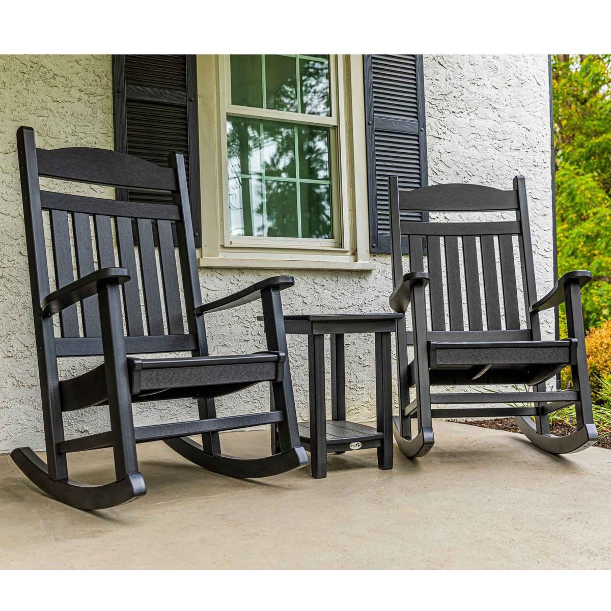 Two black poly porch rockers flanking a small side table outside a stucco house with shutters