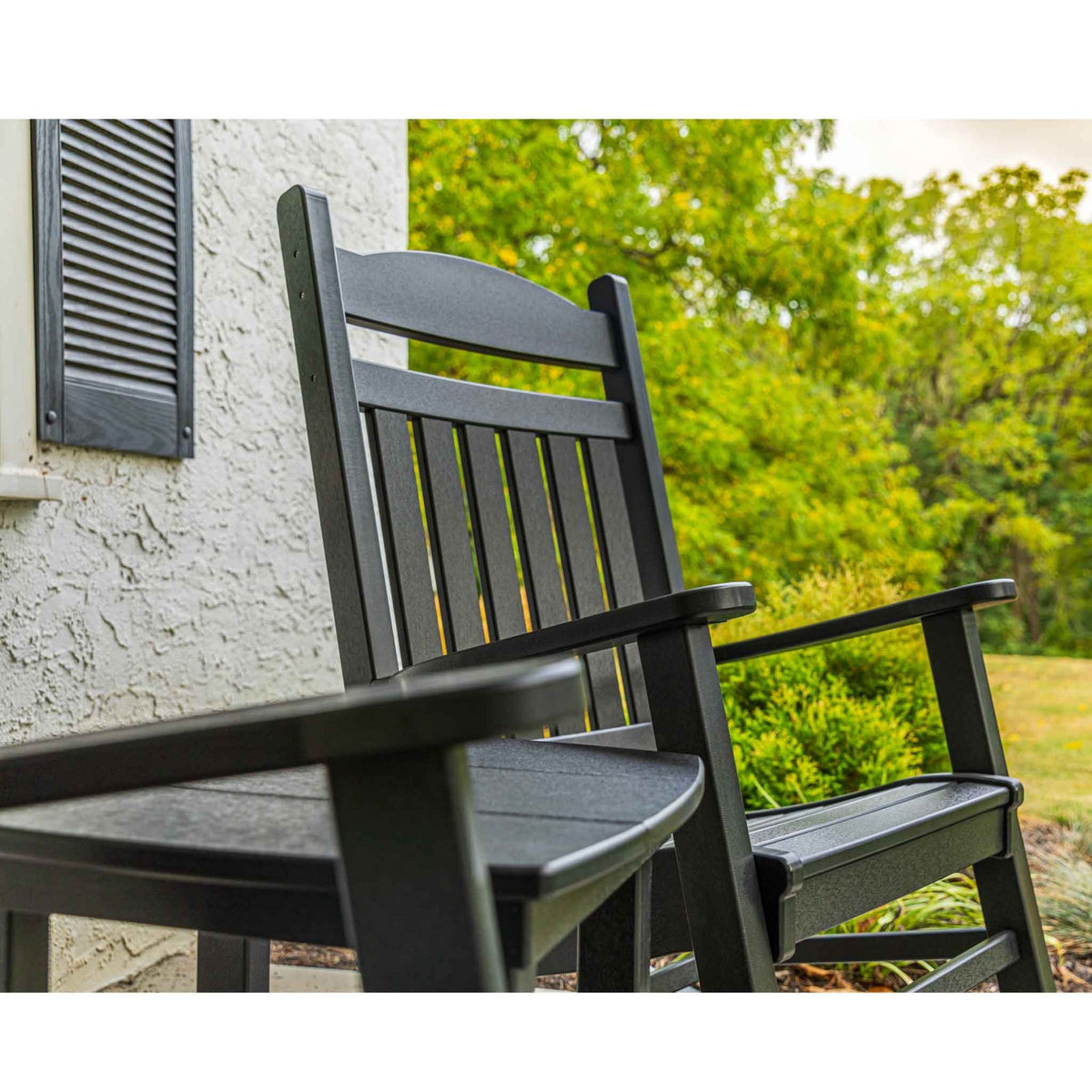 Angled view of a black poly porch rocker with an arched crest and slat back beside a side table