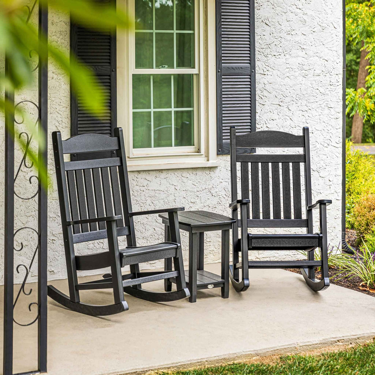 Two black poly rocking chairs with a matching side table on a front porch with black shutters