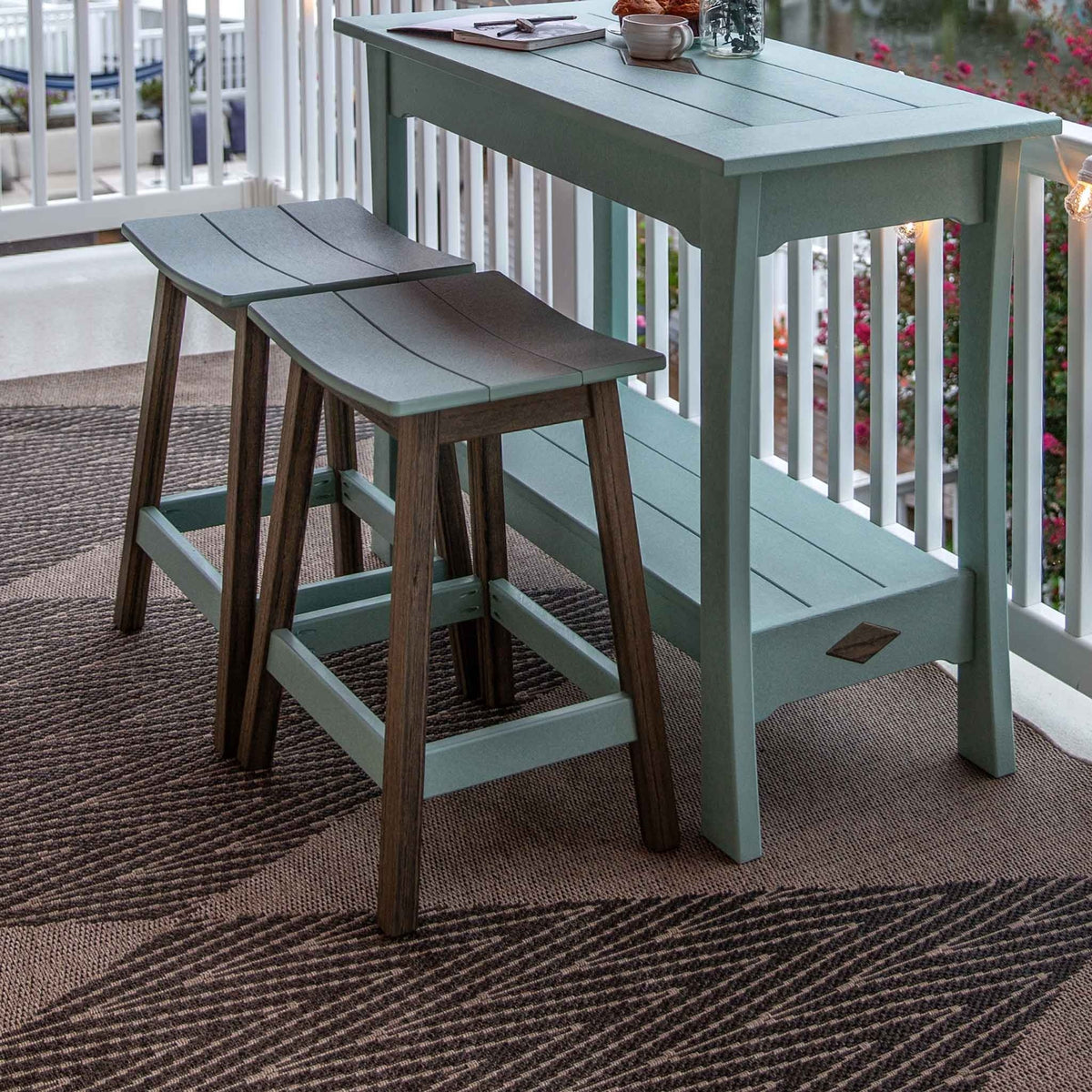 Aquamarine poly bar table with lower shelf and two saddle stools with brown legs on a patterned outdoor rug