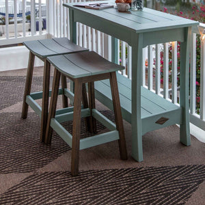 Aquamarine poly bar table with lower shelf and two saddle stools with brown legs on a patterned outdoor rug