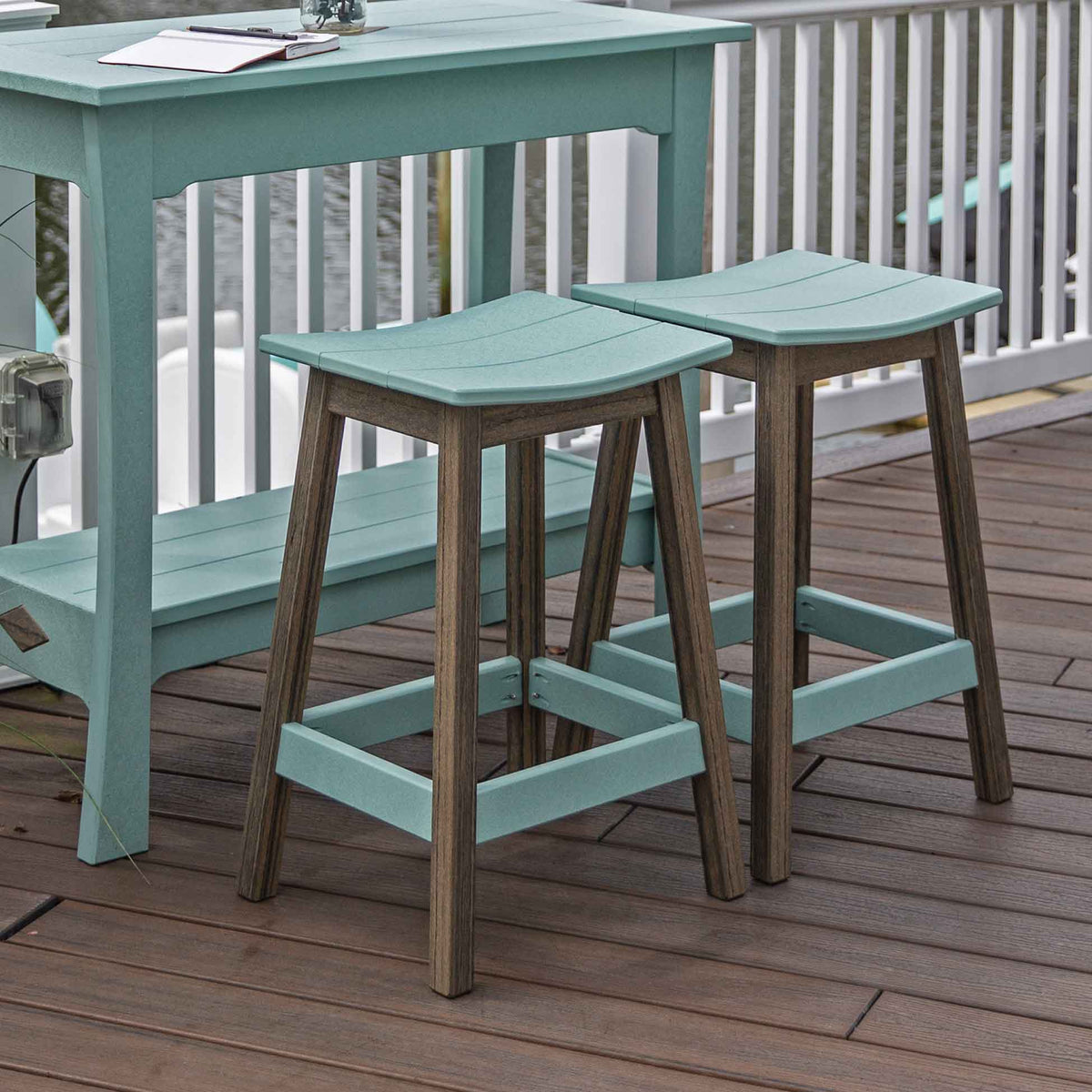 Two aquamarine saddle stools with dark driftwood legs beside a matching poly console bar table on a porch deck