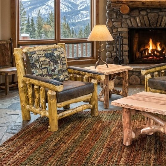 A rustic lodge-style living room featuring a stone fireplace, log furniture, and large windows with mountain views. The room includes a log chair, log sofa with patterned cushions, a log coffee table, a side table, and a woven area rug.