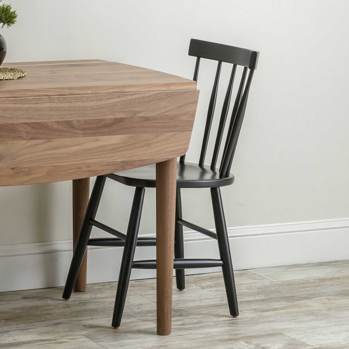 Black Windsor chair with slim back spindles pulled up to a walnut drop leaf table's rounded corner