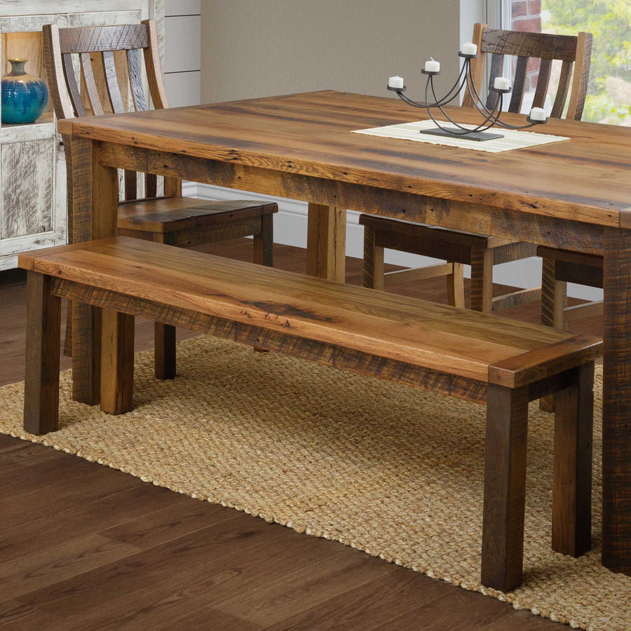 Reclaimed wood bench pulled up to a matching farm dining table with slat back chairs on a jute rug