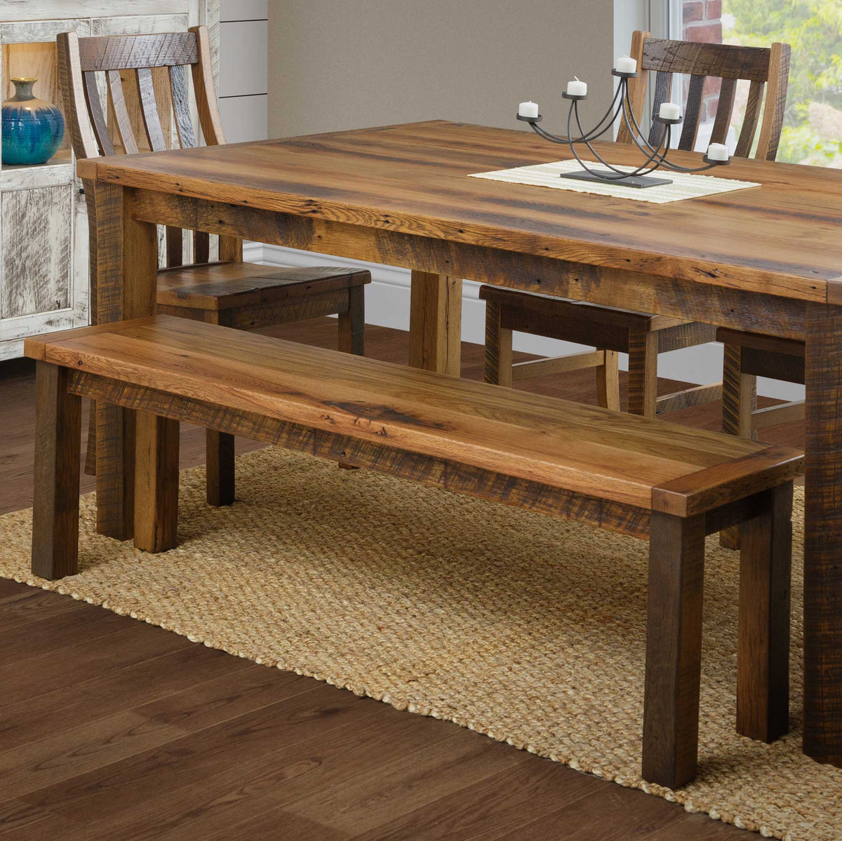 Reclaimed wood bench pulled up to a matching farm dining table with slat back chairs on a jute rug