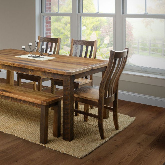 Reclaimed wood dining table with curved slat back chairs and a bench in a sunlit room with a jute rug