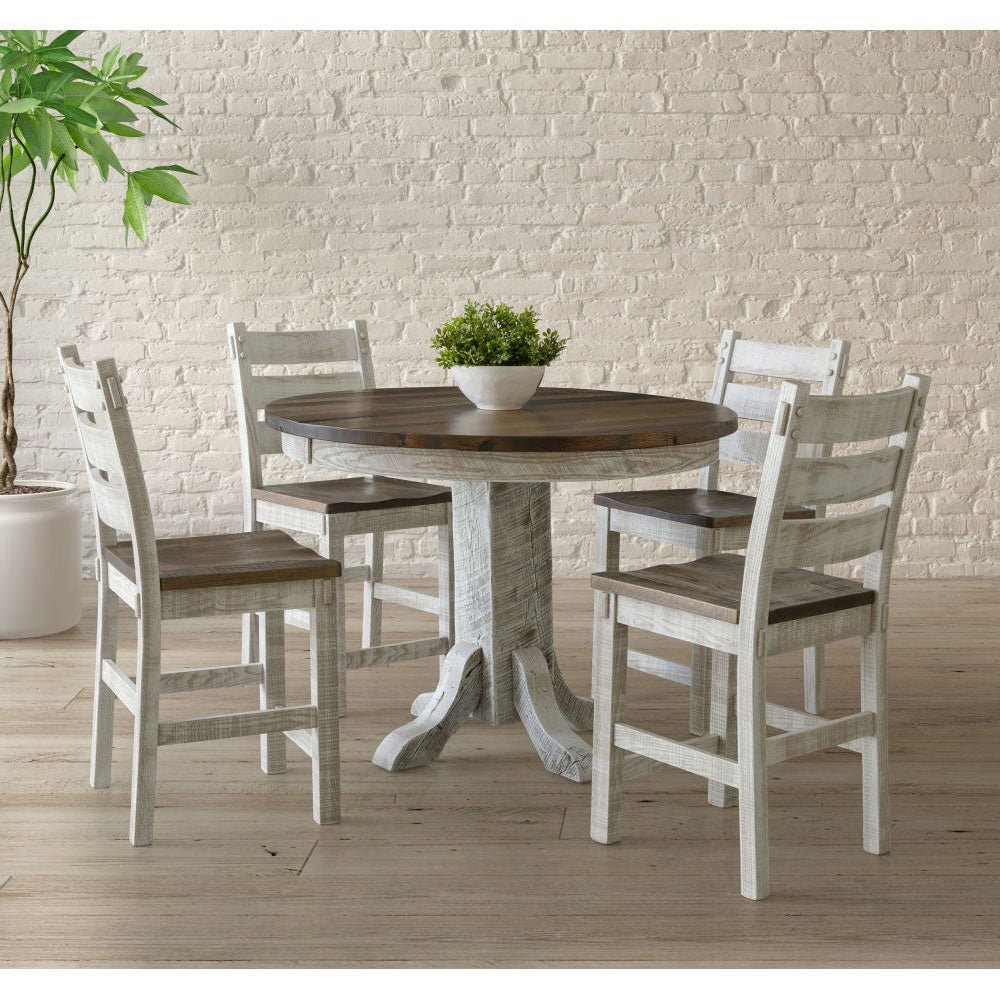 White pedestal counter table with a brown top and four tall ladder back stools against a white brick wall