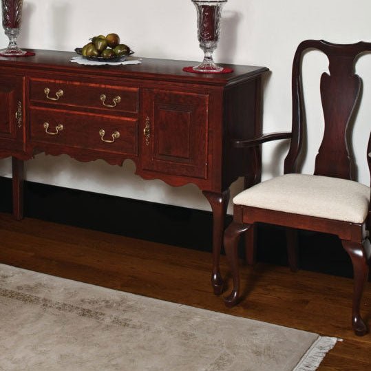 Queen Anne cherry arm chair with a cream fabric seat standing beside a matching sideboard with brass pulls