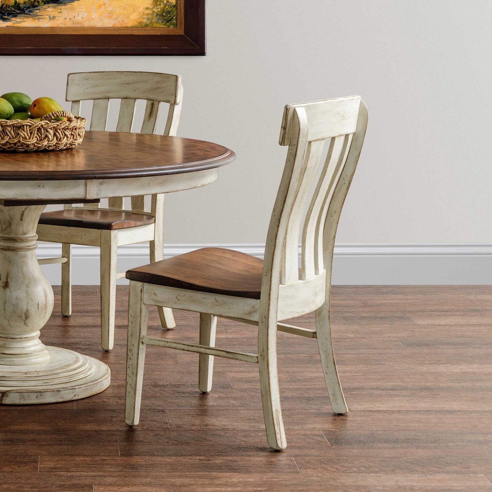 Antique white dining chair with curved slat back and warm brown wood seat, shown beside a round pedestal table in a farmhouse dining room