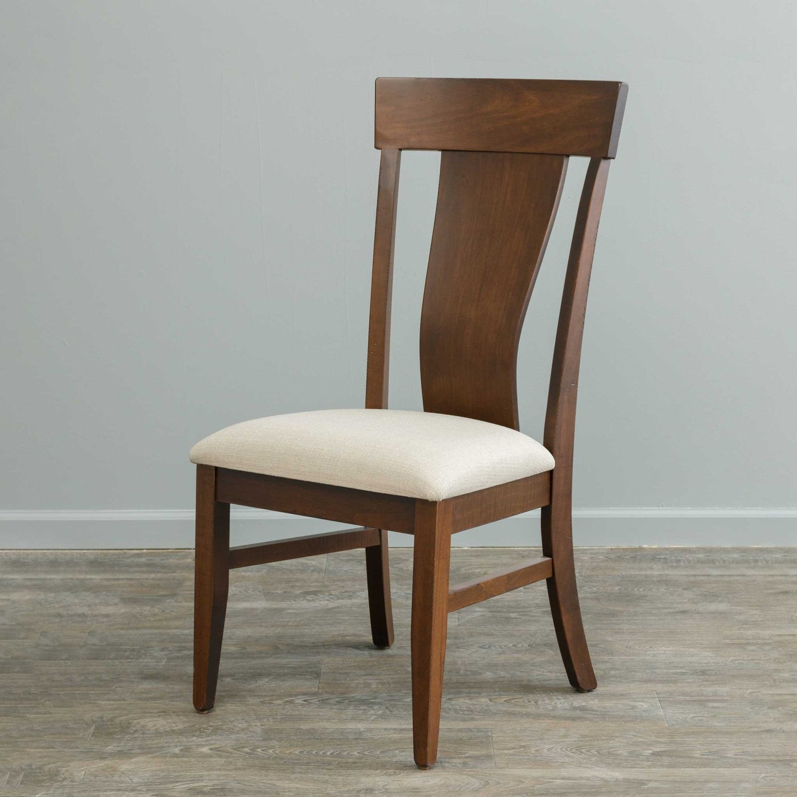 Cherry finished dining arm chair with a curved splat back and shaped arms, pulled up to a dark pedestal dining table by a draped window