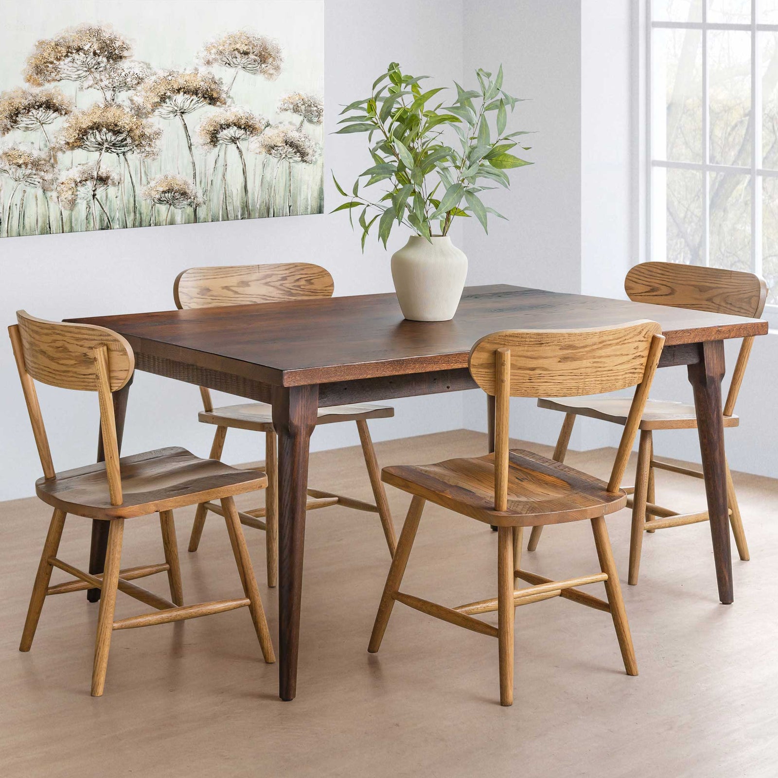 Walnut toned reclaimed dining table with four light oak round back chairs in a room with floral art