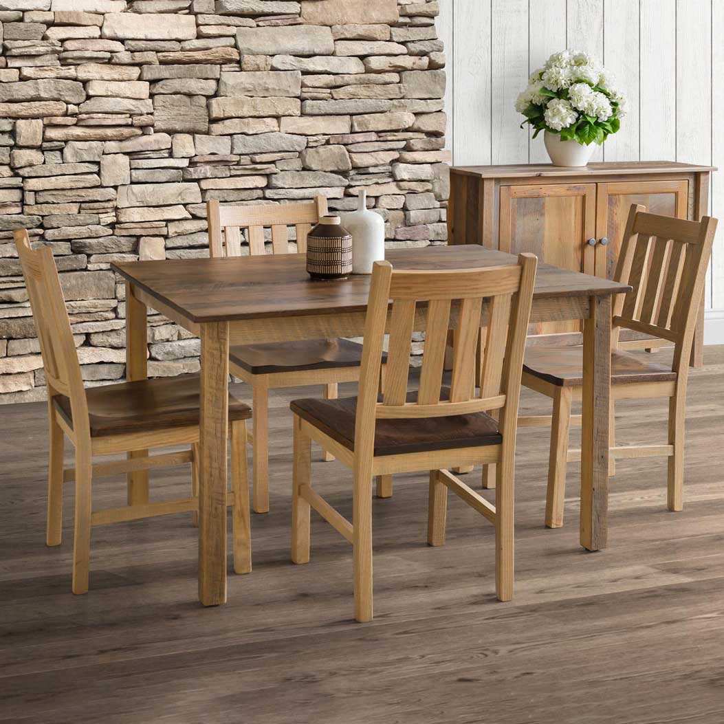 Natural finish farmhouse dining set with four slat back chairs and a cabinet against a dry stone wall