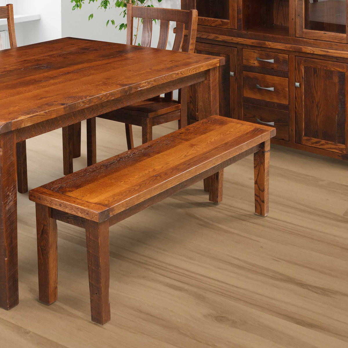 Rustic reclaimed oak dining bench in a warm medium stain, pictured beside a matching farmhouse table and sideboard buffet