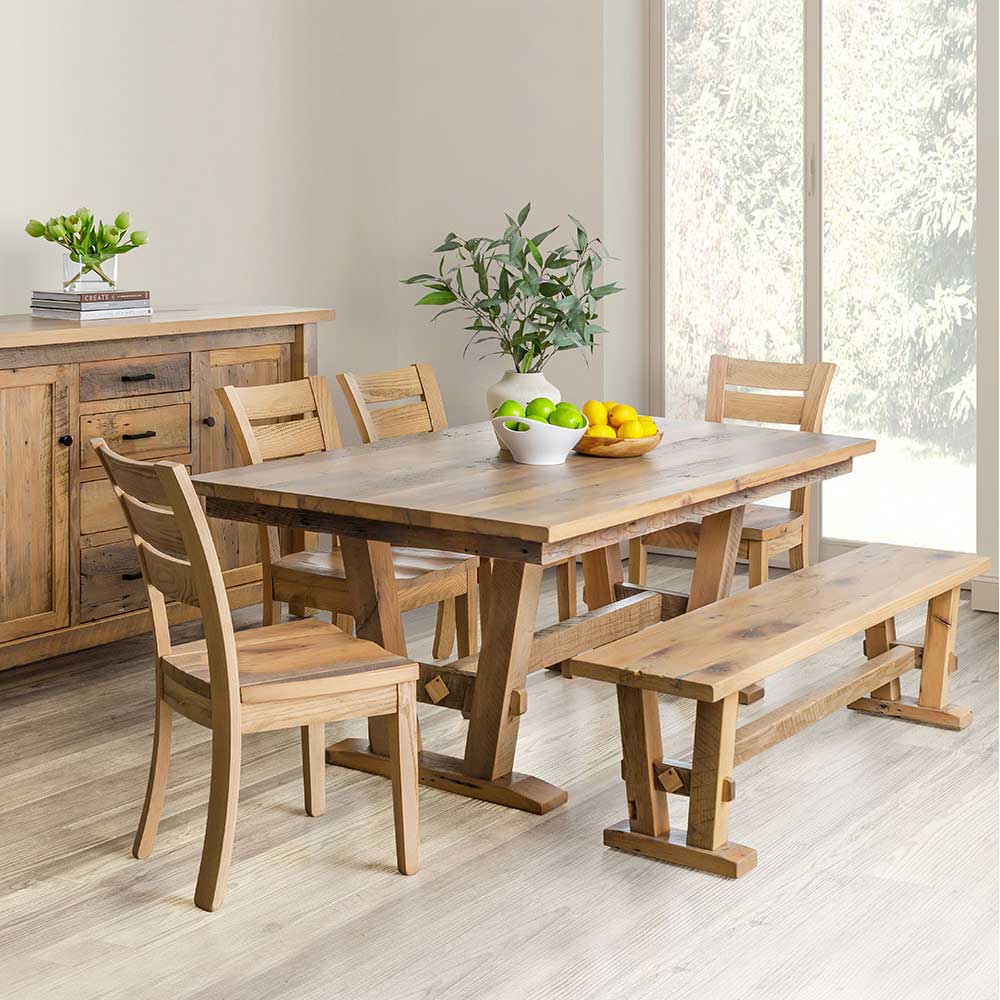 Light natural reclaimed wood dining set staged with a bench, four slat back chairs and rustic sideboard beside a sunny patio door