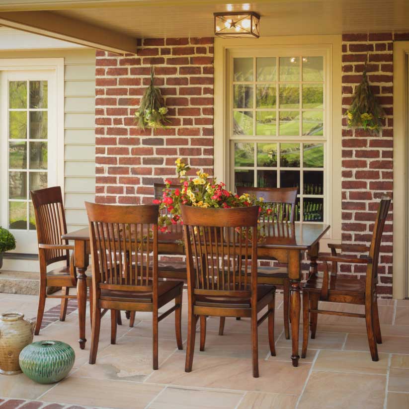 Rectangular leg extension dining table with six slat back chairs set on a brick and flagstone porch