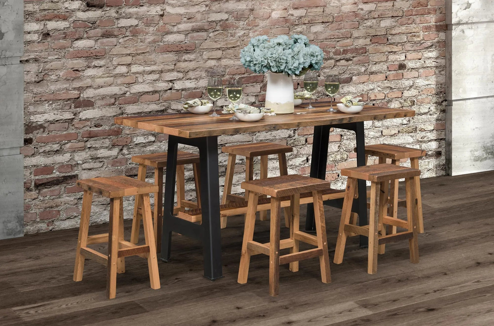 Reclaimed wood pub table with black A-frame legs and six saddle-seat bar stools against an exposed brick wall