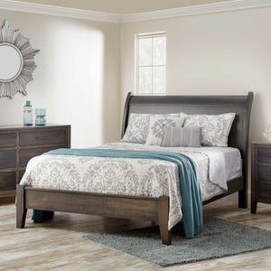 Gray finished sleigh bed with a low curved headboard, dressed in a gray floral quilt and teal throw in a light modern bedroom