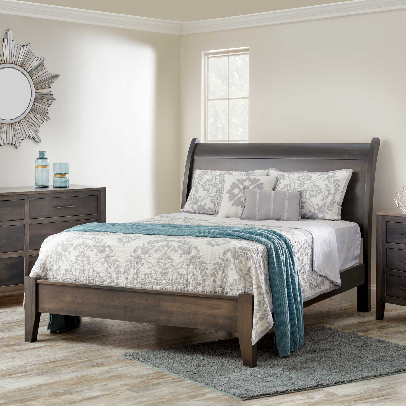 Gray finished sleigh bed with a low curved headboard, dressed in a gray floral quilt and teal throw in a light modern bedroom