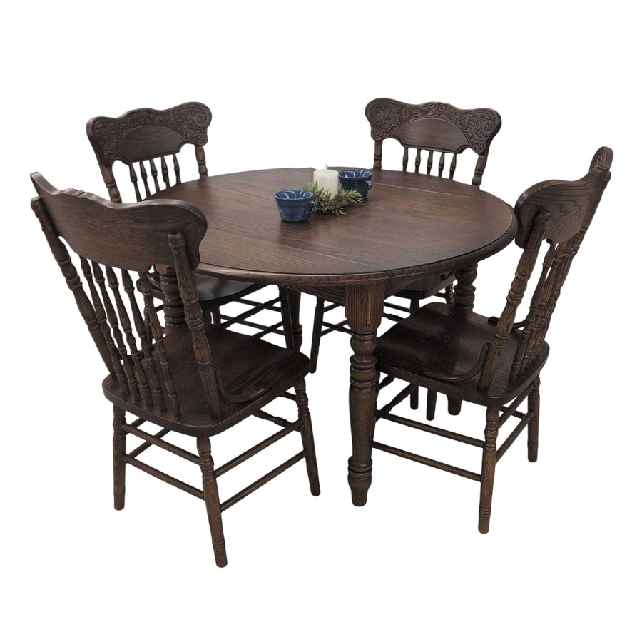 Dark stained oak round drop leaf table with four carved pressback spindle chairs, candle and blue bowls on top