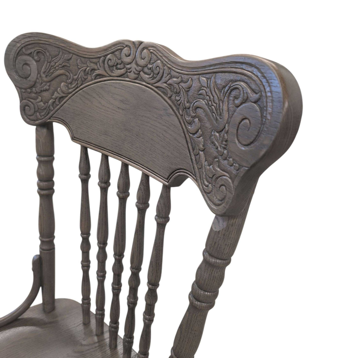Close view of the embossed scrollwork crest and turned spindles on a gray finished pressback chair