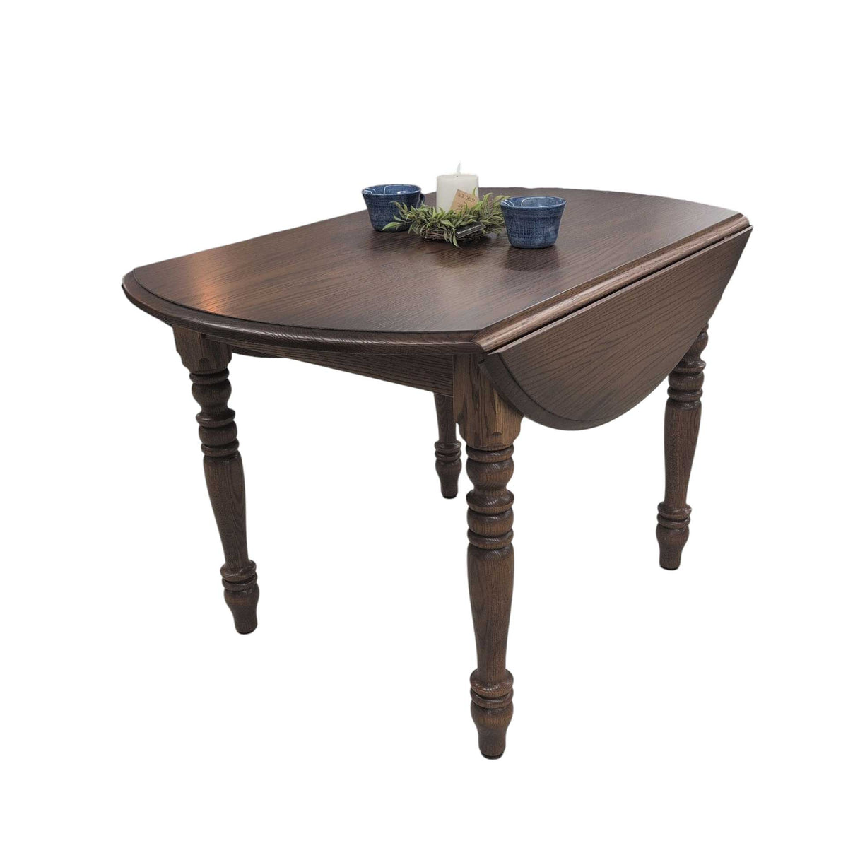 Dark oak drop leaf dining table with one rounded leaf folded down, turned legs and a candle centerpiece