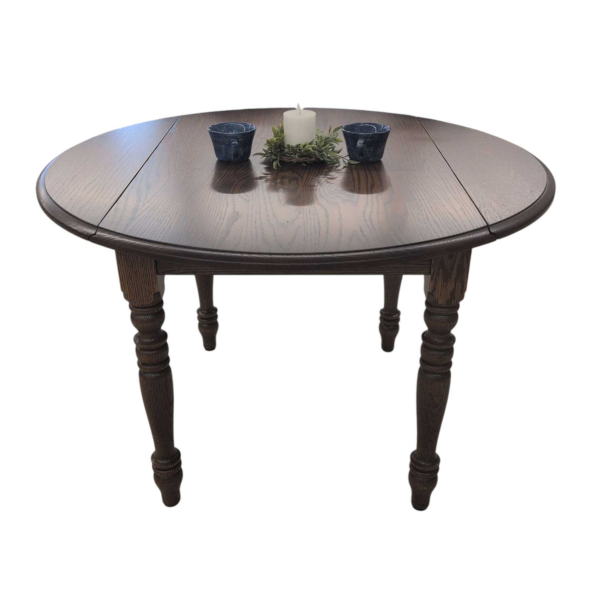 Overhead angle of a dark oak round drop leaf table with both leaves up, turned legs, candle and greenery on top