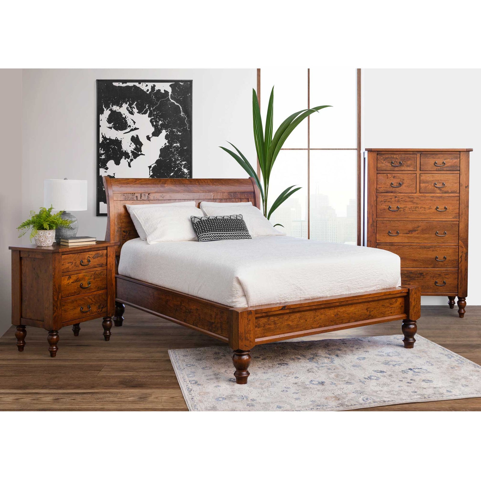 Rustic cherry bedroom set in a styled room with sleigh bed, turned legs, three drawer nightstand and tall chest