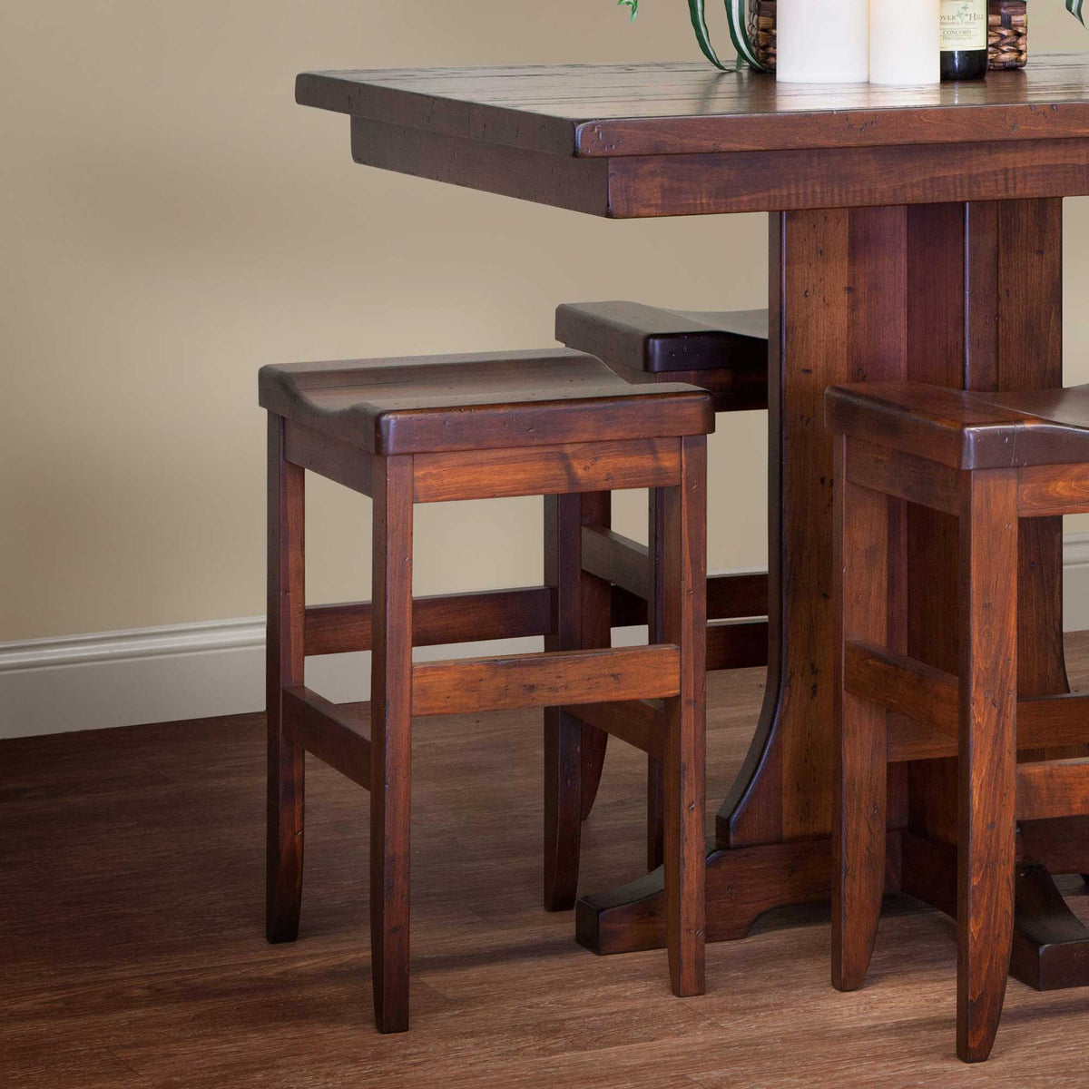Two cherry stained backless saddle stools pulled up to a rustic counter height trestle table with candles and wine