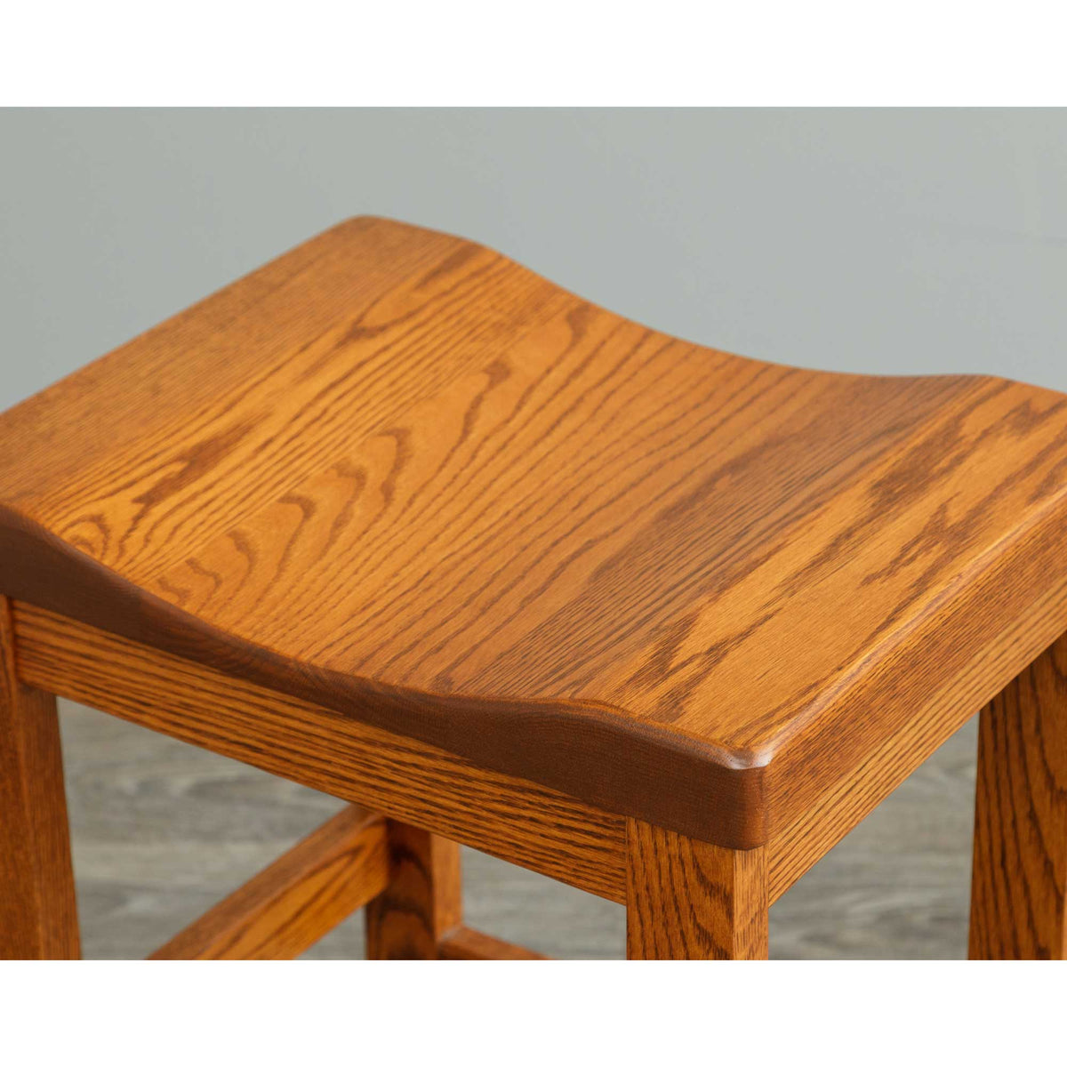 Close-up of the scooped saddle seat on an oak bar stool, showing golden brown grain and softly rounded edges