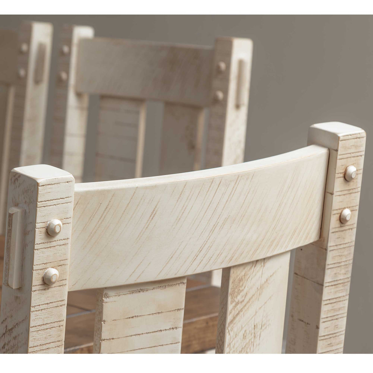 Close-up of the whitewashed dining chair back showing distressed sawn grain, curved crest rail and metal bolt accents