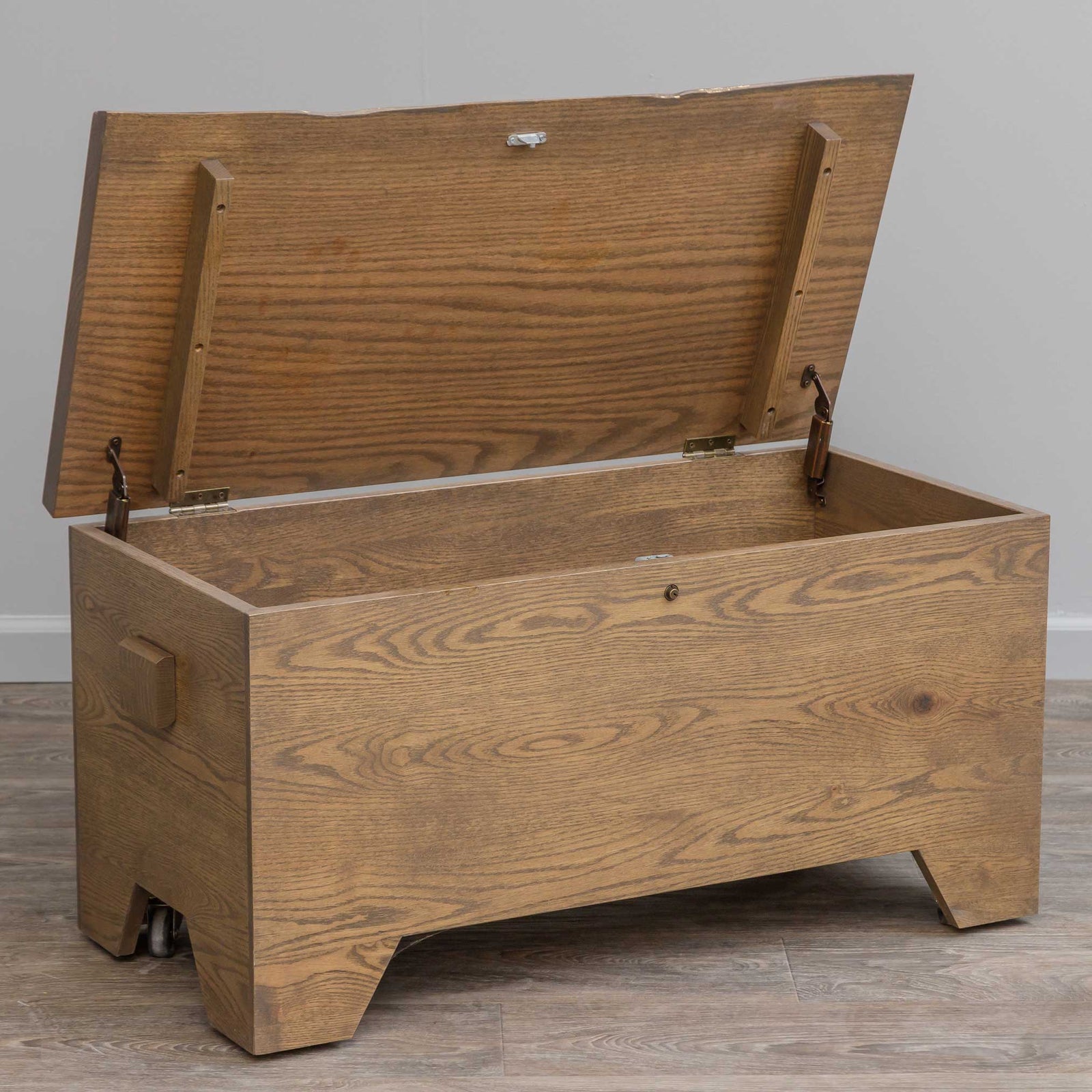 Rustic oak live edge hope chest with a plank lid, side handle and cutout bracket feet on gray flooring
